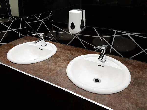 浴室内部为黑色和白色 圆形陶瓷洗脸盆 厕所后洗手用的镜子 塑料肥皂盘和镀铬水龙头 使用深色瓷砖进行设计 — 图库照片