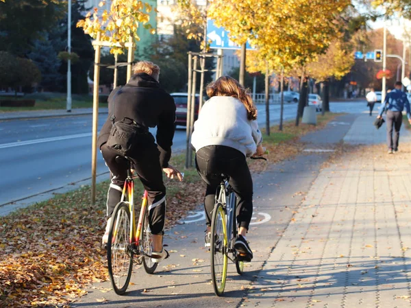 A young couple, a guy and a girl, ride a bike along the path through the autumn gulitsa in the daytime. Relax active life. Ride on ecological transport. Environmental protection in a European city.