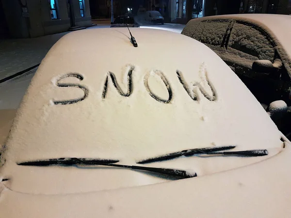 The windshield of a passenger car covered with snow, on which the word \