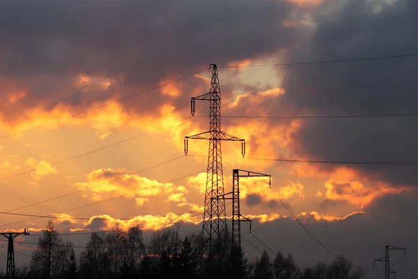 High voltage electric lines cross the hilly mestnost. Electric station in the summer under the open sky. Power industry. Ecology of nature. Metal technological structures. Strategic object in sunset