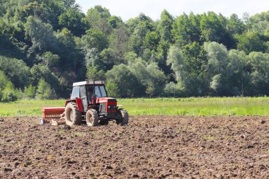Bir çiftçi bir sembol ile kırmızı bir traktör tahıl köyü alan özel bir alanda sürülmüş topraklarda sows. Mekanizasyon bahar saha çalışması. Çiftçinin günlük yaşam. Toprak işleme. Tarım