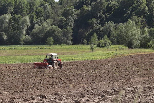 在乡村地区的一个私人田地里 一个农夫在一辆红色拖拉机上用播种机播种谷物 春季野外作业机械化 农民的日常生活 处理土地 的土地 — 图库照片