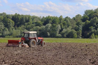 Bir çiftçi bir sembol ile kırmızı bir traktör tahıl köyü alan özel bir alanda sürülmüş topraklarda sows. Mekanizasyon bahar saha çalışması. Çiftçinin günlük yaşam. Toprak işleme. Tarım