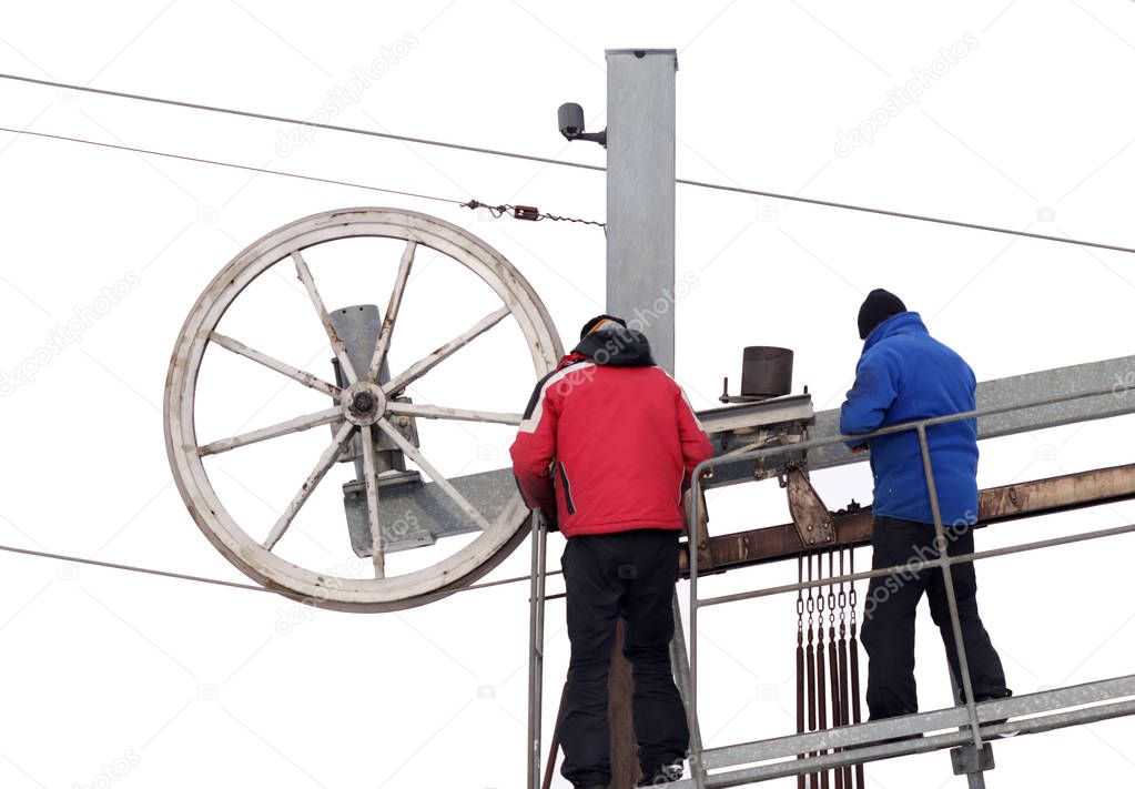 Two workers of the ski lift repair the spinning mechanism of the lower station. Repair work on a winter resort. The product and construction of metal. Professional knowledge. Towing with steel ropes.