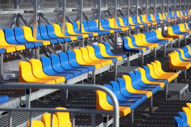 Yeni mavi ve sarı plastik sandalyeyle metal hafif yapı futbol sahası üzerinde duruyor. Stadyumda hayranları için yerler. Spor karşılaşmaları için seyirci olacak. Belgili tanımlık koşmak--dan sığınak.
