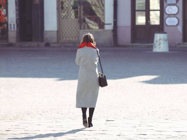 Bir kadın bir şık sonbahar kıyafeti antik kentin kaldırımda yürüyor. Güzel manken doldurma kırmızı gri ceket. Serbest zaman, eser dinlenmek. Neşeli ve sakin ruh hali
