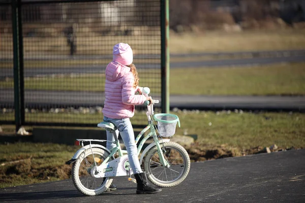 Девушка в полусезонной одежде с розовым оттенком едет на велосипеде по асфальтовой дороге. Молодое поколение занимается спортом и активно проводит свободное время на свежем воздухе. Игры на улице — стоковое фото