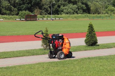 Turuncu mekanik cihaz temizlik ve çim oluşumunu nesneleri bir yeşil futbol sahası, koşu bandı, çalılar ve ağaçlar arka planı açık havada spor. Yeşil teknoloji çalışma