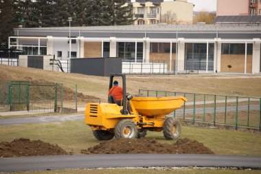 Bir işçi bir küçük turuncu damperli kamyon üzerinde taşıma ve Spor Stadyumu manzaraya oluşturan yere boşalma. Benford ekipman Kazı çalışmaları. Futbol fiel topraklarında hareketi