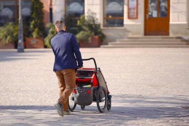 Şehir merkezinden yürüme bir modern turistik bebek arabası olan bir çocuk ile genç bir adam. Genç nesil yetiştirme sorumluluğunu baba. Aile tatili. Yavru Bakımı