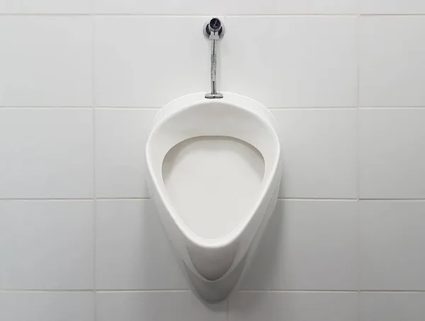 Wnętrze łazienki wyłożone są białymi płytkami ceramicznymi. Owalny pisuar ceramiczny. Miejsce publiczne na potrzeby radzenia sobie z potrzebami. Ceramiczny produkt gospodarstwa domowego. Oszczędzając bieżącą wodę w codziennym życiu. Rozwiązanie do projektowania toalety — Zdjęcie stockowe