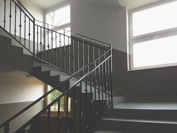 A staircase with forged cast-iron railings in a modern building illuminated with light from the windows. Interior staircase and escape route during a cataclysm. The design of the room in gray tones