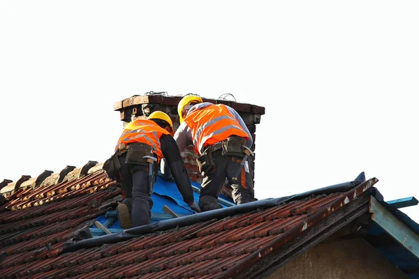 Dois construtores em roupas de trabalho consertando um telhado de azulejos velho em um prédio. Trabalhos de construção em altura sobre um fundo branco isolado para posterior projecto. Equipamento de segurança profissões de alta altitude — Fotografia de Stock