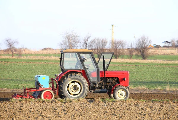 Kırmızı traktörlü bir çiftçi ve tohum ekici köy bölgesindeki özel bir tarlaya tahıl ekiyor. Bahar alan çalışmalarının mekanizasyonu. Çiftçinin günlük hayatı. insan emeğinin kolaylığı