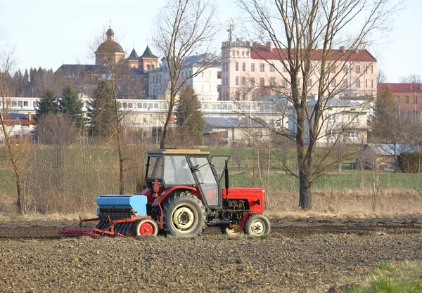 一位农民开着一辆红色拖拉机，用播种机播种谷物，播种在村子里的一块私人田里。春田工作机械化。法默的日常生活。人的劳动救济 — 图库照片