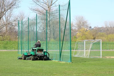 Büyük yeşil bir çim biçme makinesindeki işçiler futbol sahasındaki çimleri biçerler. Spor kompleksinin yeşil alanlarının peyzaj tasarımı ve bakımı. Maçtan önce çimen stadyumu yapıyorum. İnsan emeği
