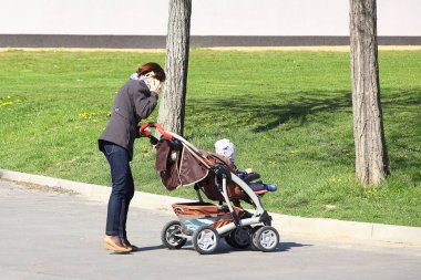 Bebekli genç bir anne cep telefonuyla konuşuyor. Oğlu ya da kızı olan bir kızı gezdir. Sosyal ağlara ve modern teknolojilere bağımlılık. İnsanlar arasında mobil iletişim.