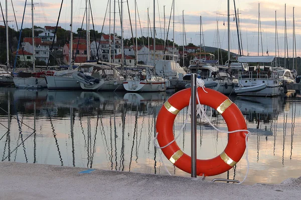 Oranžový život prsten na molu v chorvatské Marině na pozadí plachetní jachty. Bezpečnost na vodě a uložení utonutí. Zařízení přístavu. Oblečení ze záchranného týmu — Stock fotografie
