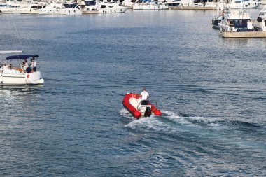 Marina staf yat limanına giren bir yelken Cruise yat için kırmızı şişme motorlu tekne üzerinde yelken. Bir charter tekne palamar ile pilot yardım. Muhafız tarafından geminin doğrulama