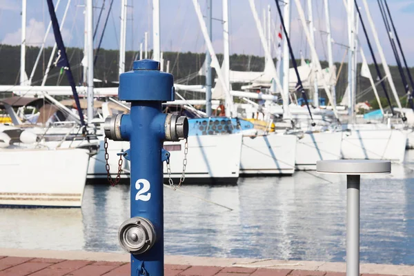 Гідравлічний пожежний кран синього кольору на набережній пристані на тлі припаркованих вітрильних яхт. Пожежна безпека порту і вуглецевих чартерних човнів. Боротьба елементами — стокове фото