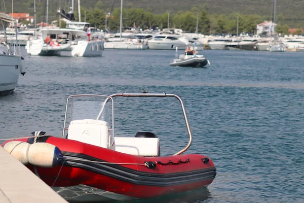The red inflatable motor boat is moored to the pier in the background of the marina with yachts. Pilot ship to assist in the mooring of ships. Dingy staf. Infrastructure of the Mediterranean port