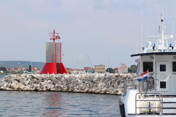 En stor kustbevakning båt står i en småbåtshamn nära en vågvatten med en röd fyr. Polis skepp vid ingången till hamnen. Bokstavliga skyltar för ingången till hamnen. Navigationssäkerhet. — Stockfoto