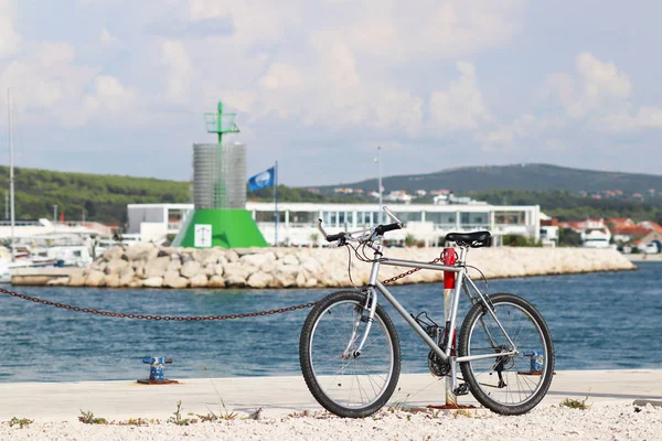 The bike is parked on the pier of the Mediterranean marina on the background of the signal beacon in green. Urban ecological mode of transport. Infrastructure Dalmatian Riviera. Vacation