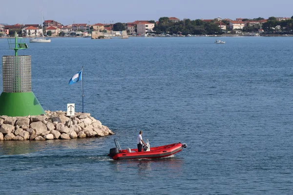 Людина в надувному моторному човні, плаває повз кам'яній воді з небезпечним сигналом маяка. Відпочинок на воді в раю. Середземноморський круїз на чартерному судні. Пілот та персонал Марина — стокове фото