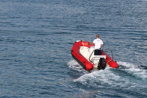 O staf marina está navegando em um barco a motor inflável vermelho para um iate de cruzeiro à vela que entra na marina. Assistência de pilotagem com a amarração de um barco fretado. Verificação do navio pela guarda — Fotografia de Stock