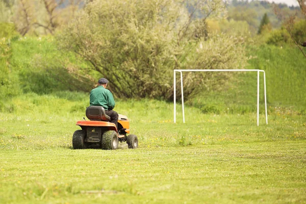Werknemer op een grote groene grasmaaier maait het gras op het voetbalveld. Landschapsontwerp en onderhoud van groene zones van het sportcomplex. Het maken van gras stadion voor de wedstrijd. Menselijke arbeid — Stockfoto