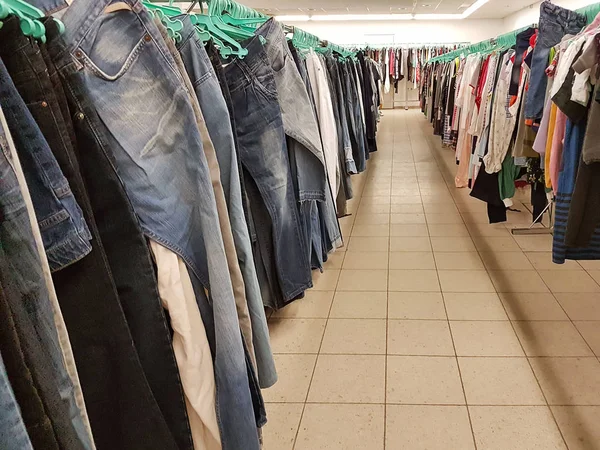 Les vêtements pèsent sur les cintres dans un magasin d'occasion. Achat de jeans et chemisiers pas chers d'occasion dans la cabine. Des choses à la mode dans une situation économique de crise. Échange de marchandises du textile — Photo
