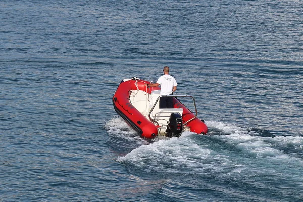 Стаф яхты плавает на красной надувной моторной лодке к парусной круизной яхте, входящей в пристань. Помощь пилота при швартовке чартерного судна. Проверка судна охранником — стоковое фото