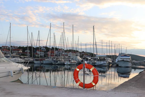 Orange life ring on the pier in the Croatian marina against the backdrop of sailing yachts. Safety on the water and saving drowning. Equipment of the seaport. Outfit of the rescue team