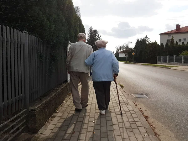 Um par de idosos caminham ao longo da calçada ao longo da estrada de mãos dadas. Avô e avó em uma caminhada em uma área residencial. Movimento saúde dos idosos. Velha idade feliz — Fotografia de Stock