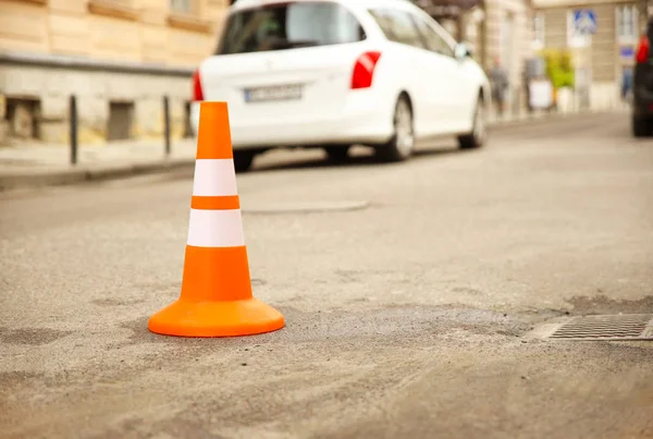 Reparação sinal de trabalho restringindo o tráfego. Branco-laranja plástico listrado cone aviso de perigo. A apertar no trânsito. Rua da cidade velha com carros. Reparação de estradas. Pobre asfalto na estrada. Atenção! — Fotografia de Stock