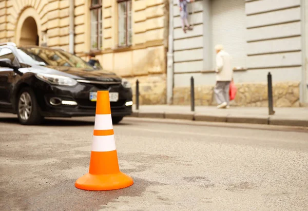 Reparação sinal de trabalho restringindo o tráfego. Branco-laranja plástico listrado cone aviso de perigo. A apertar no trânsito. Rua da cidade velha com carros. Reparação de estradas. Pobre asfalto na estrada. Atenção! — Fotografia de Stock