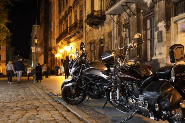 Chrome elements of stylish motorcycles in the lights of the ancient evening city of Lviv in Ukraine. Tourist trip of bikers. Profitable parking for choppers. Evening cheerful life of youth
