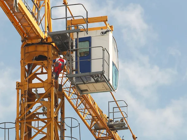 在一幢多层建筑的施工过程中，工装裤的起重机工人正在修理正在施工的一座高层塔式起重机。高风险的工作在高处。吊起重型建筑材料。城市发展. — 图库照片