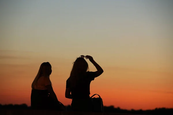 The dark power of two girls against the backdrop of a crimson sunset. A play of colors and darkness. Photographing in the dark with low light. Girlfriends romantically relax in the evening