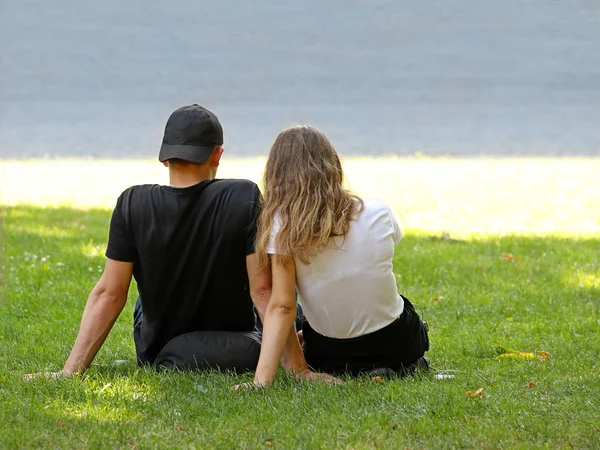 一个和一个女孩坐在海边草地上的家伙。夏天在大自然中浪漫约会的恋人。男人和女人之间的关系。编织手。呆在一起青少年之间的爱情 — 图库照片