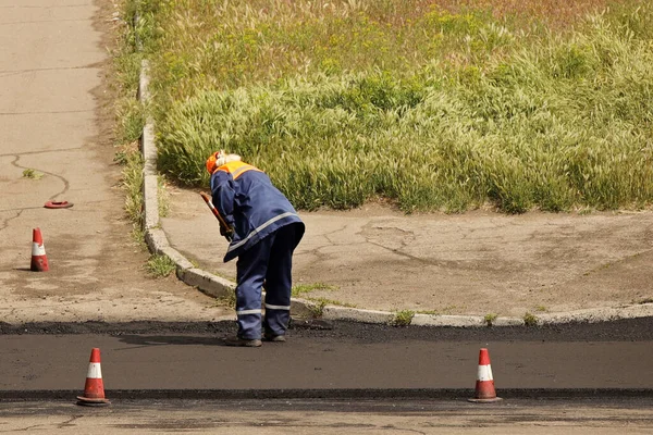 Laying asphalt by workers. Road construction. Modern technology of laying a highway with a solid surface. People work at a construction site. The worker is leveling the surface manually.