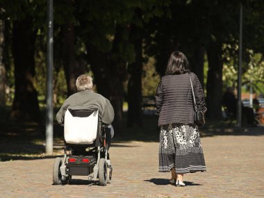 Bir kadın, elektrikli sandalyede seyahat eden bir adamla parkta yürüyor. İhtiyaç sahiplerinin velayeti. Kısıtlı hareket kabiliyetine sahip insanların faaliyetleri. Kas iskeleti sistemi hastalarının protezleri..
