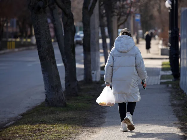 一个带着包裹的女人在阳光灿烂的人行道上走着 城市街道上的行人 一个女人在家里的日常生活 去商店购物的旅行 用塑料袋在上面 — 图库照片