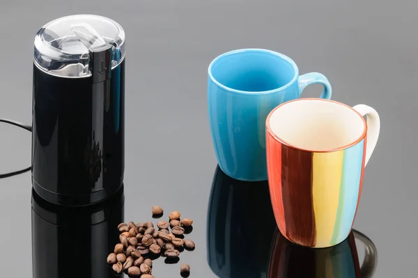 Moedor de café com grãos de café e caneca no backg espelho cinza — Fotografia de Stock
