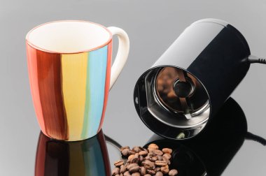 Gri ayna arka üzerinde kahve fasulyesi ve kupa ile çay değirmeni