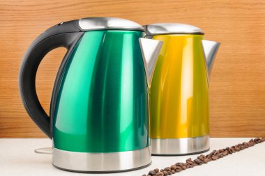 Ahşap üzerinde avuç kahve çekirdekleri ile iki elektrikli su ısıtıcıları ve