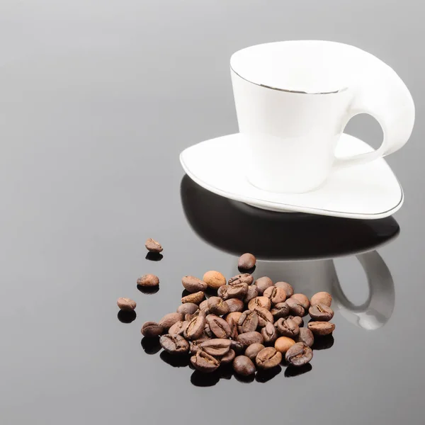Taza de café blanco con granos de café sobre el fondo gris espejo — Foto de Stock