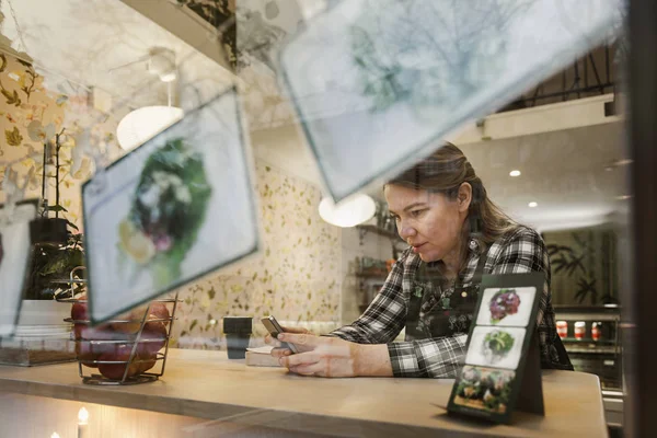 Mujer que utiliza smartphone en la cafetería, vista a través del cristal. - foto de stock