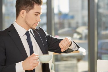 Zamanlama her şeydir. Bir fincan kahve tutarak saati zamanında kontrol yakışıklı genç işadamı