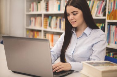 Üniversite Kütüphanesi'nde çalışan gülümseyerek, onu laptop, yazarak çekici kendine güvenen kız öğrenci. E-öğrenme programı zevk mutlu güzel kadın. İstihbarat, uluslararası eğitim kavramı